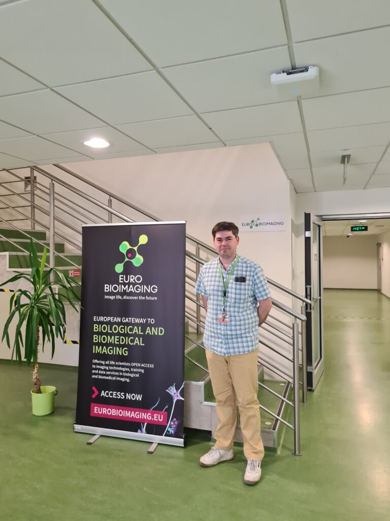 Michal Mikal, Head of the Brno Node and Representative of medical imaging within node in front of the Euro-BioImaging poster in the facility.